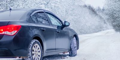 Schwarzes Fahrzeug fährt im Winter auf einer verschneiten Straße.