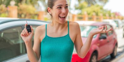Glückliche junge Frau hält einen Autoschlüssel in der Hand.