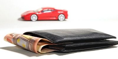Geldbörse mit Geldscheinen sowie kleines rotes Auto im Hintergrund.