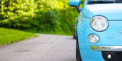 Türkisfarbener Fiat 500 fährt auf einer Landstrasse im Wald.