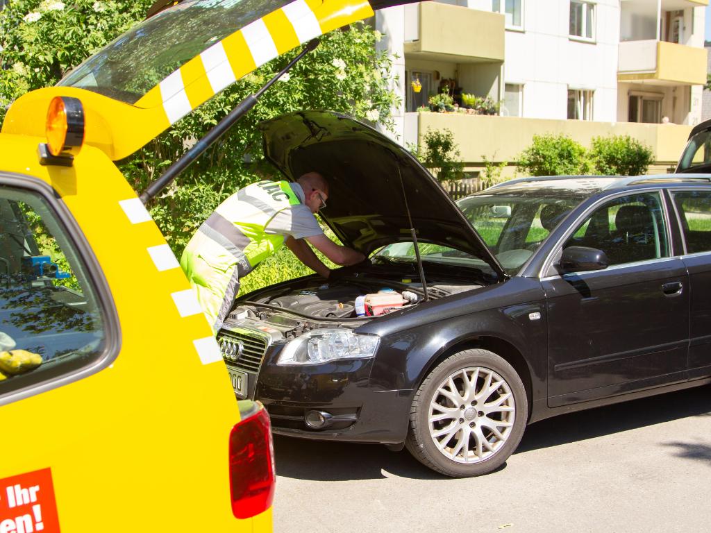 Mitarbeiter der Pannenhilfe schaut in den Motorraum eines defekten Fahrzeugs.