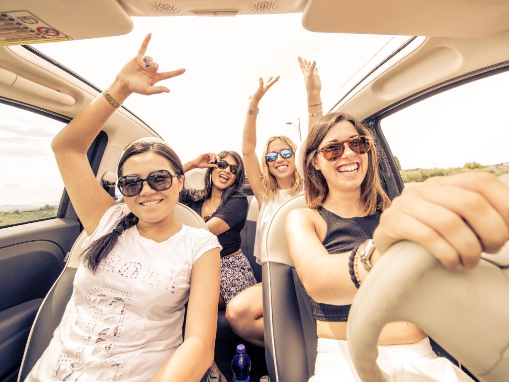 Gruppe junger Frauen fahren im Cabrio und heben die Hände vor Freude.