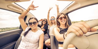 Gruppe junger Frauen fahren im Cabrio und heben die Hände vor Freude.