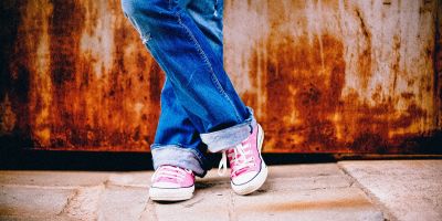 Frau trägt blaue Jeans und pinkfarbene Chucks und schlägt die