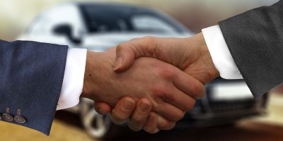 Zwei Geschäftsmänner schütteln sich die Hand vor einem Auto, um