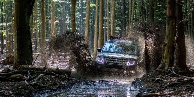 Geländewagen fährt durch einen Feldweg im Wald, der unter Wasser steht.
