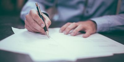 Ein Mann im Hemd unterzeichnet Dokumente mit einem Stift.