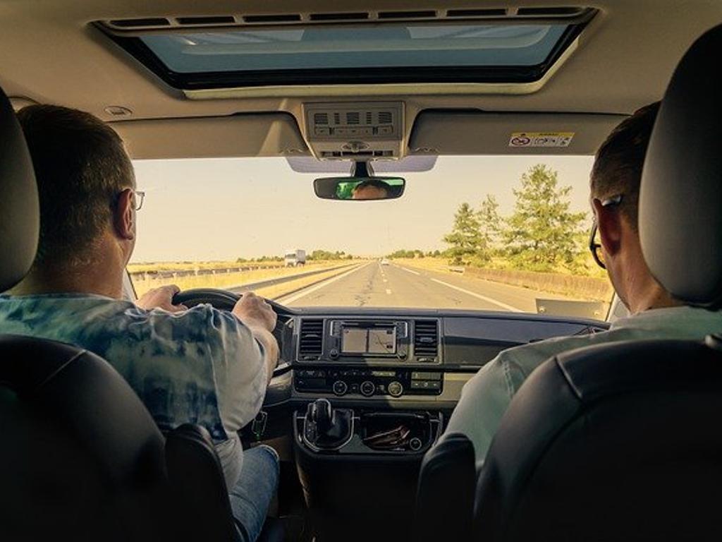 Zwei Personen sitzen im Auto und fahren über eine Bundesstrasse.